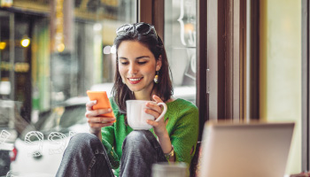 A young woman sitting in a cafe using a cell phone.