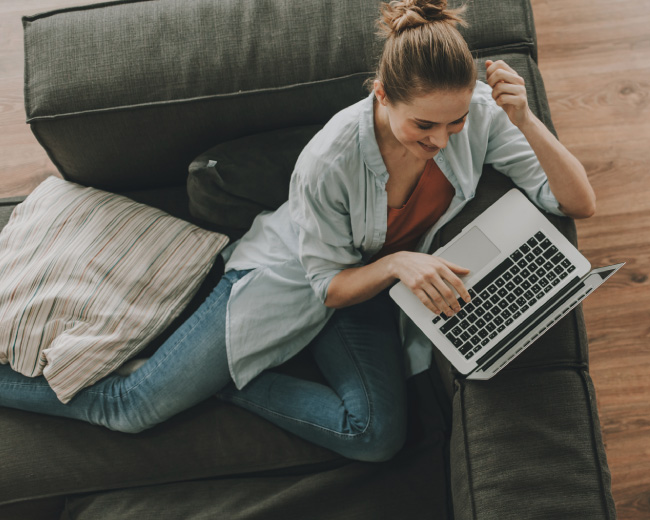 Overhead view of a woman laying on a couch with a laptop.