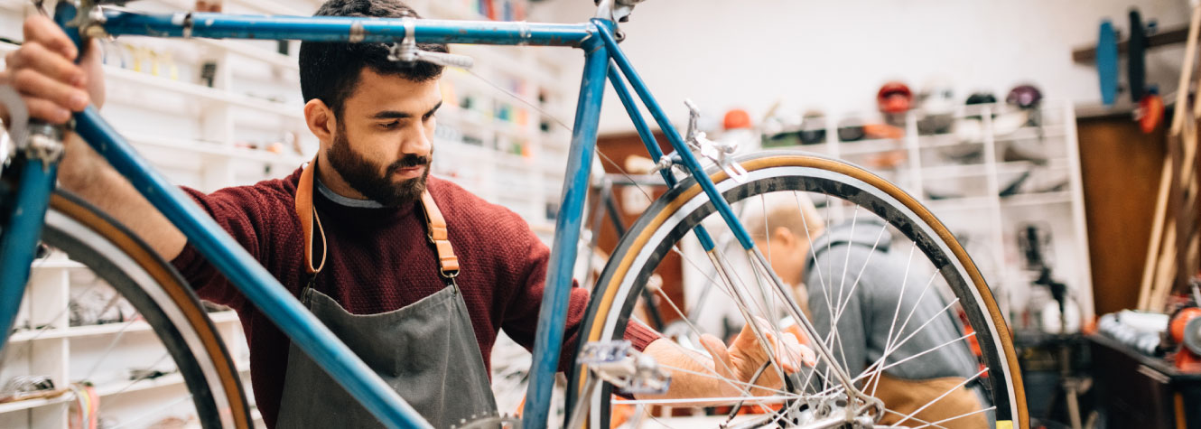 A man in an apron working on a blue bycicle.