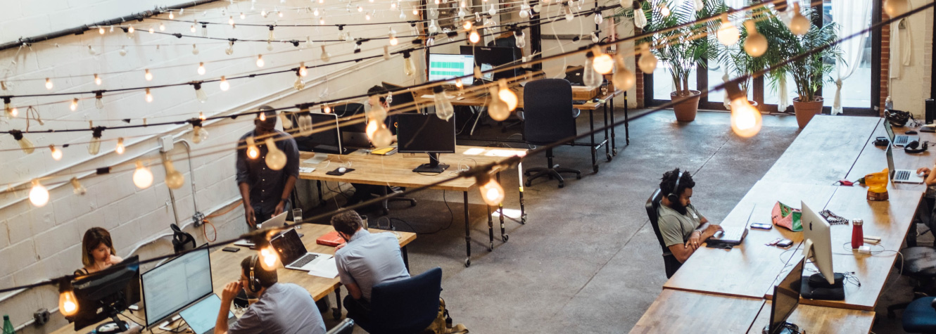 Overhead view of a trendy office with multiple people sitting with laptops and monitors.