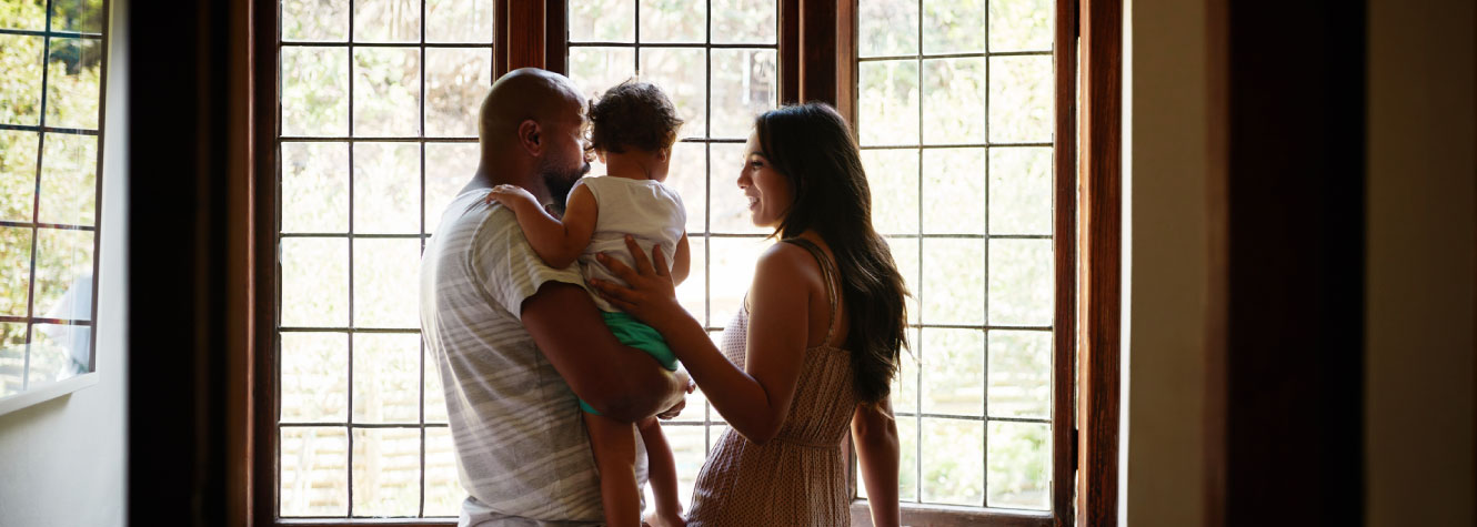 A young family looking out a large window inside a house.