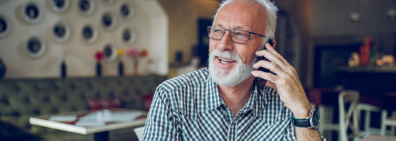 An older man sitting in a restaurant talking on a cell phone.